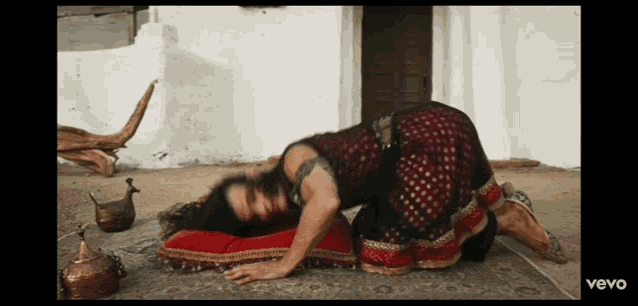 a woman in a red and gold dress is kneeling on the ground with the word vevo on the bottom left