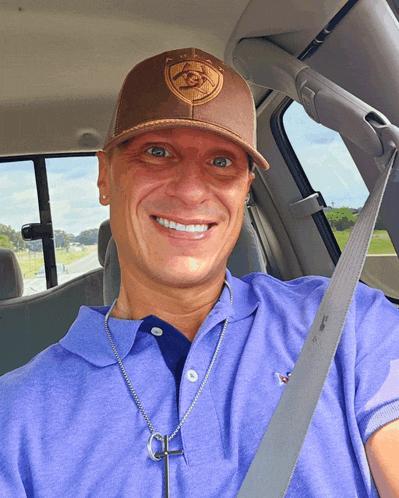 a man wearing a purple shirt and a brown hat is smiling in the back seat of a car