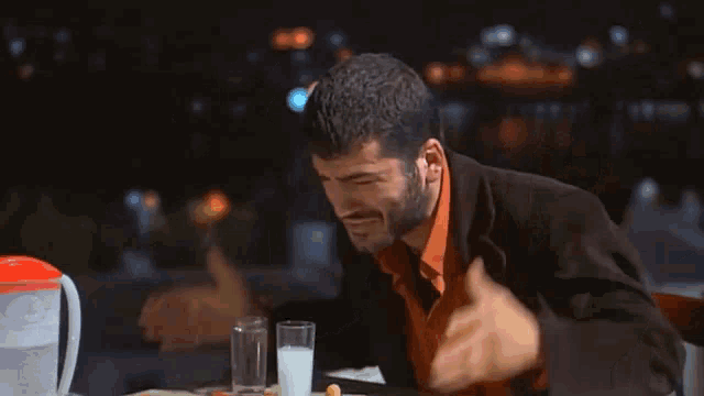 a man with a beard is sitting at a table with a pitcher of water and two glasses of milk .
