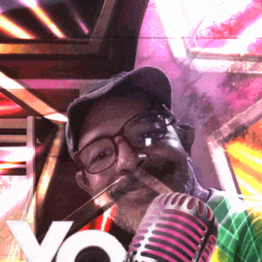 a man wearing glasses and a hat holds a pink microphone in his mouth