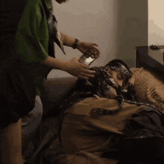 a man with a bandana on his face is laying on a bed with a cat