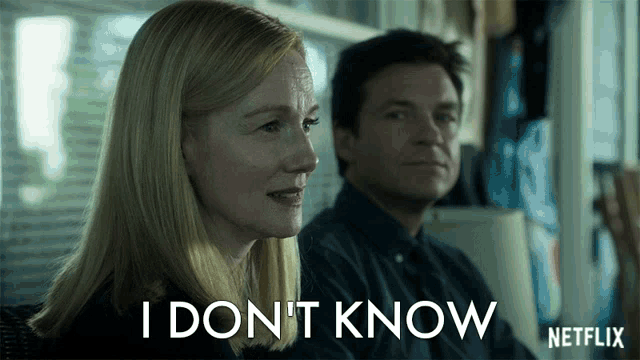 a man and a woman are sitting in front of a sign that says " i don t know "