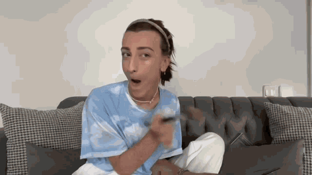 a man in a blue tie dye shirt is sitting on a couch with a spoon in his mouth .
