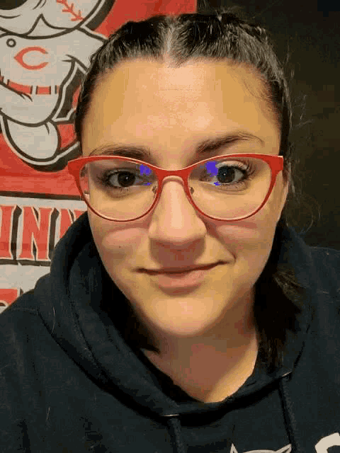 a woman wearing red glasses and a black hoodie stands in front of a cincinnati cubs banner