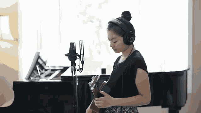 a girl wearing headphones is playing a guitar in front of a microphone