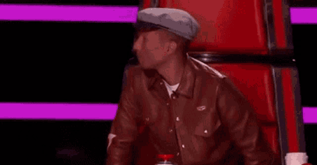 a man wearing a hat and a brown leather jacket is sitting in a chair .