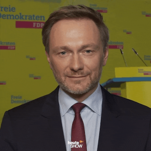 a man in a suit and tie stands in front of a yellow wall that says freie demokraten fdp