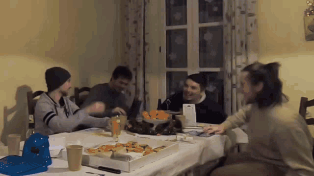 a group of people are sitting at a table with a box of food on it