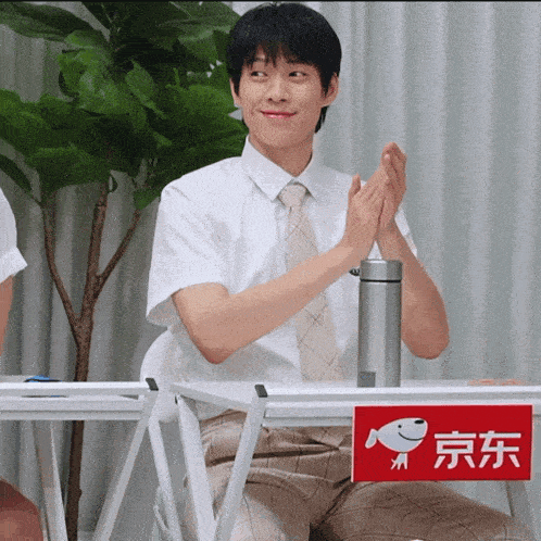 a man in a white shirt and tie sits at a table with a sign on it that says ' jd '