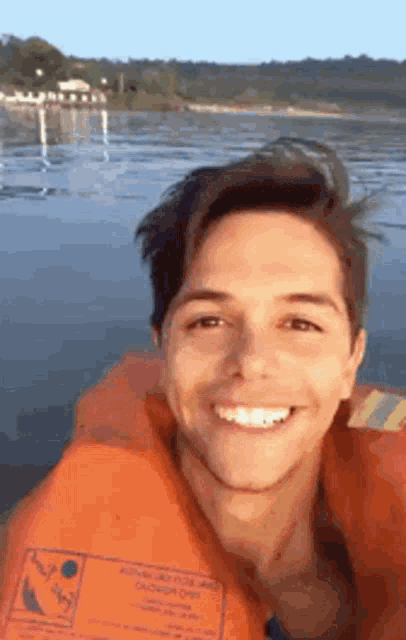 a young man wearing an orange life jacket is smiling while sitting in a boat .