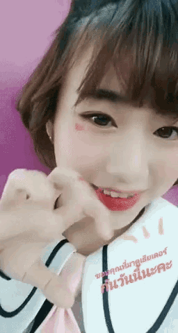 a girl is making a heart shape with her hand on her face
