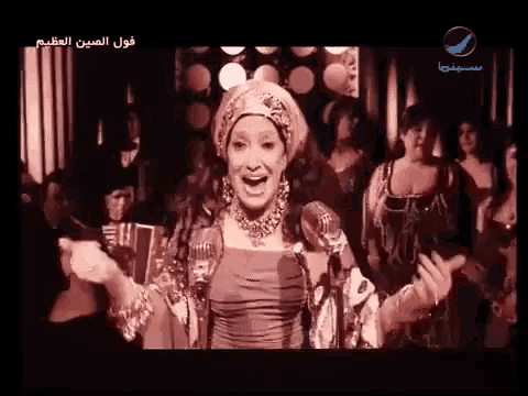 a woman singing into a microphone in front of a crowd with arabic writing on the bottom
