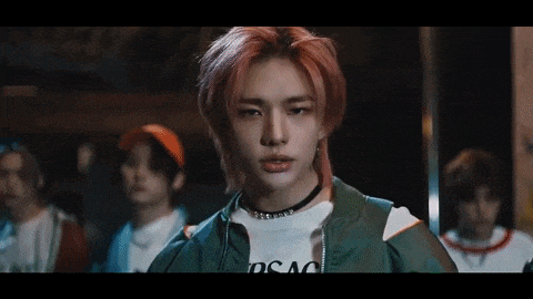 a young man with red hair and a choker is standing in front of a group of young men .