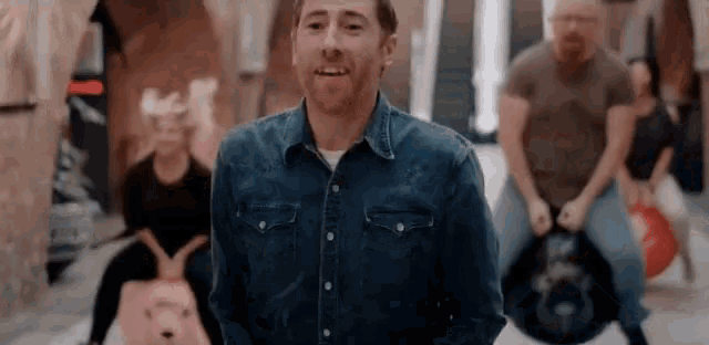 a man in a denim shirt is standing in front of a group of people riding balloons .