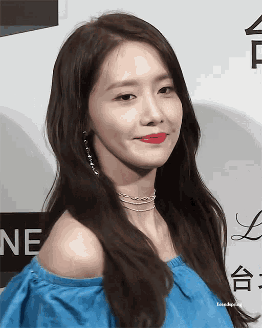 a woman wearing a blue off the shoulder top and red lipstick is standing in front of a sign that says ne