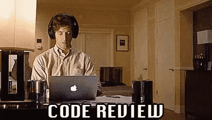 a man wearing headphones is sitting at a desk with a laptop computer and the words code review above him .