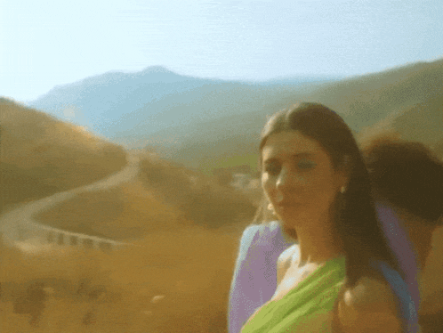 a woman in a green dress is standing in front of mountains