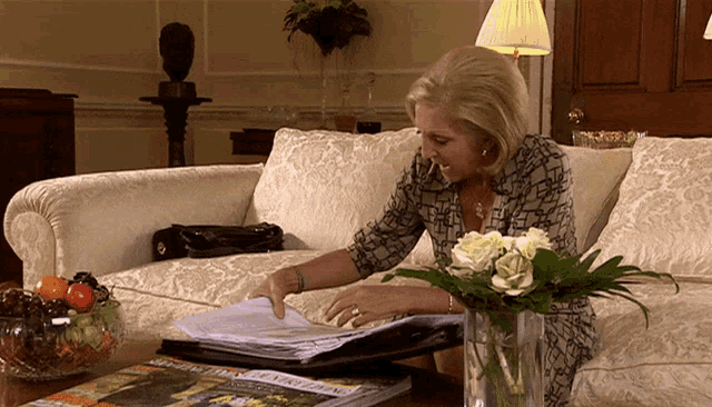 a woman is sitting on a couch looking at a stack of papers