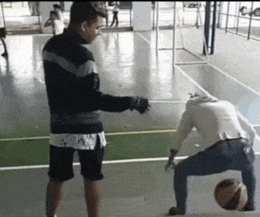 a man in a black jacket is standing next to a man in a white shirt who is kneeling down with a basketball