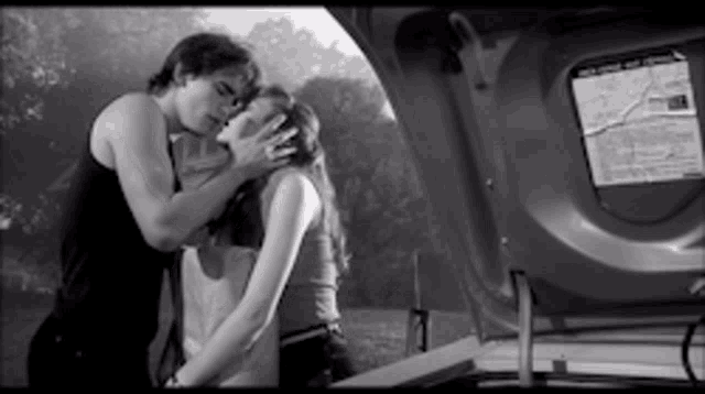 a black and white photo of a man and woman kissing in the trunk of a car