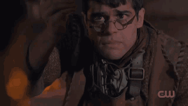 a man with glasses and a cw logo on the bottom right