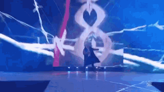 a man in a black cape is walking on a stage in front of a large screen .
