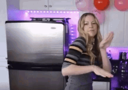 a woman is dancing in front of a stainless steel refrigerator .