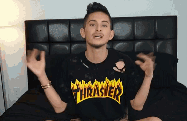 a man wearing a thrasher t-shirt is sitting on a bed