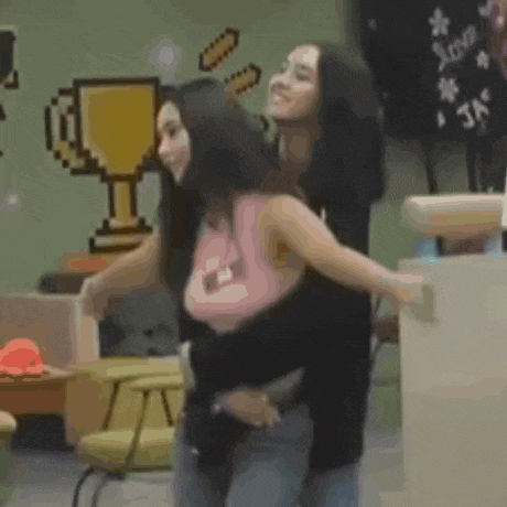 two women are hugging each other in a room with a trophy on the wall behind them .