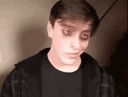 a young man with black eyes and a black shirt is making a face .