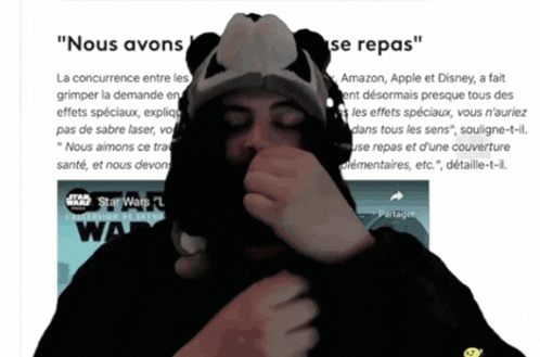 a man wearing a panda hat is covering his mouth with his hand in front of a star wars poster