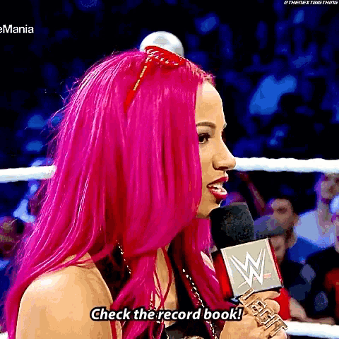 a woman with pink hair is talking into a microphone and saying check the record book .