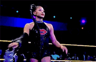 a female wrestler is standing in a wrestling ring with a crowd watching .