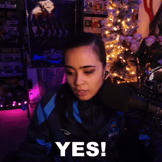a woman sitting in front of a christmas tree with the word yes on her face