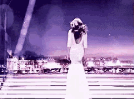 a woman in a white dress is standing on a bench in front of a city at night .