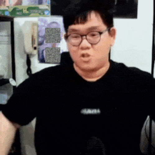 a man wearing glasses and a black shirt is talking into a microphone in a room