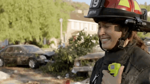 a woman wearing a firefighter 's helmet is smiling and holding a walkie talkie .