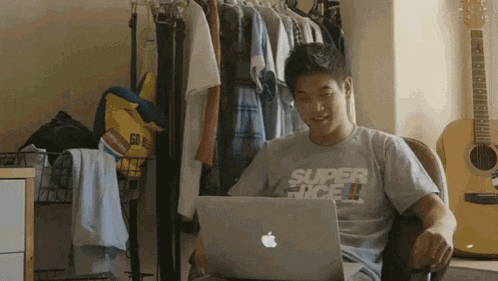 a man wearing a shirt that says super rice sits in front of a laptop