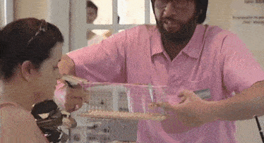 a man in a pink shirt is holding a cage with birds in it