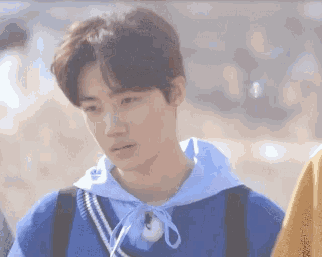 a young man wearing a blue sweater with a white ribbon around his neck