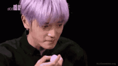 a man with purple hair is covering his face with a tissue .