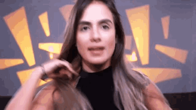 a woman in a black turtleneck is holding her hair in front of a yellow background