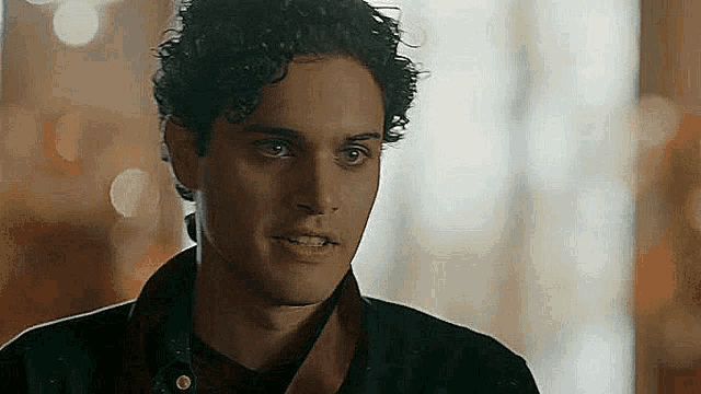 a young man with curly hair is looking at the camera in a room .