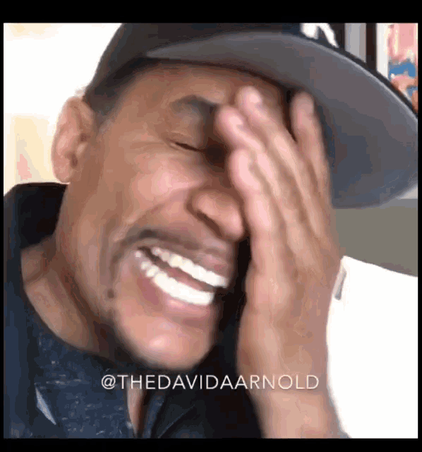 a man wearing a hat is covering his face with his hands while smiling .