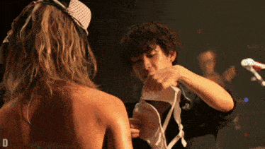 a woman in a bra is being helped by a man with the letter d in the lower right corner