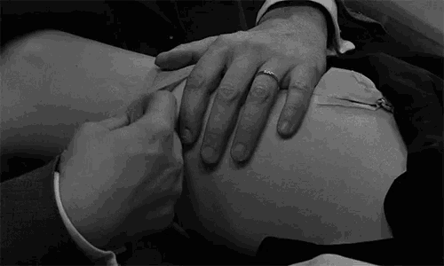 a man is touching a woman 's stomach in a black and white photo while wearing a wedding ring .