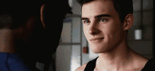 a young man in a black tank top is smiling at another young man .