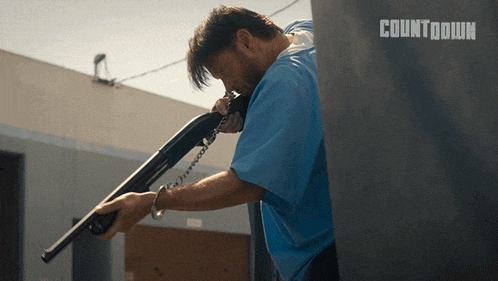 a man in a blue shirt holds a shotgun in front of a sign that says countdown