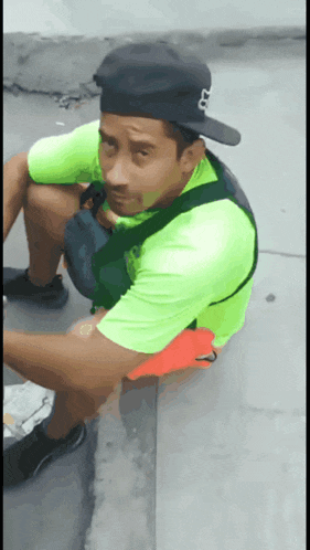 a man wearing a fox hat and a neon green shirt sits on a sidewalk
