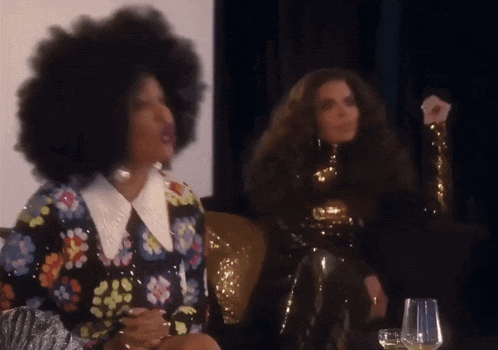 two women are sitting on a couch and one is wearing a floral dress